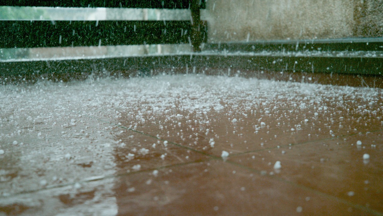 CLOSE UP, DOF: Tiny grains of soft hail fall on the wet brown tiled floor of a balcony. Raindrops and graupel falling on the wet ground during summer thunderstorm. Unpredictable springtime weather