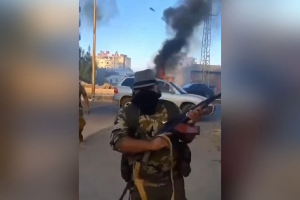 Homem armado circula em rua com veículos incendiados ao fundo durante confrontos no sul da Síria