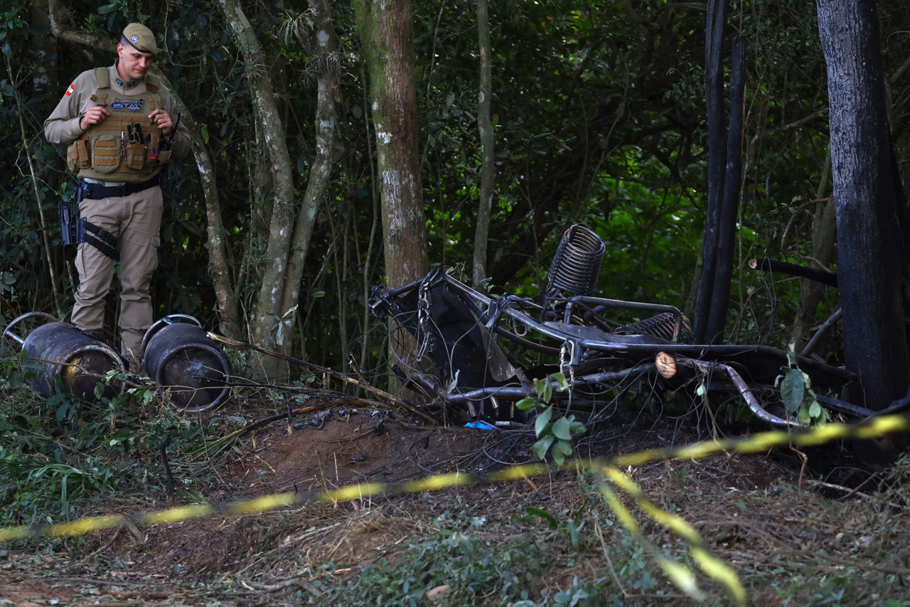 A military police officer stands next to the wreckage of a hot air balloon that caught fire and crashed with 21 people on board in Praia Grande, Santa Catarina State, southern Brazil, on June 21, 2025. At least eight people were killed and 13 others were injured after the basket plummeted dozens of meters to the ground in flames in southern Brazil, the governor of Santa Catarina, Jorginho Mello, reported. (Photo by SILVIO AVILA / AFP)