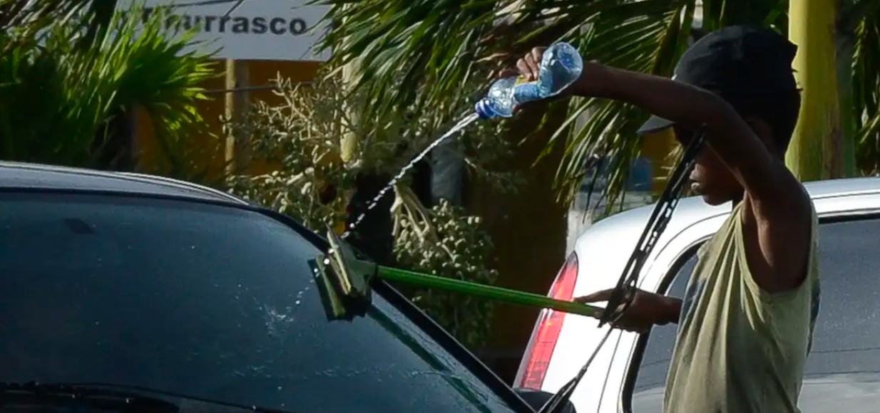 Imagem ilustrativa de um menino trabalhando como lavador de vidro de carro num semáforo