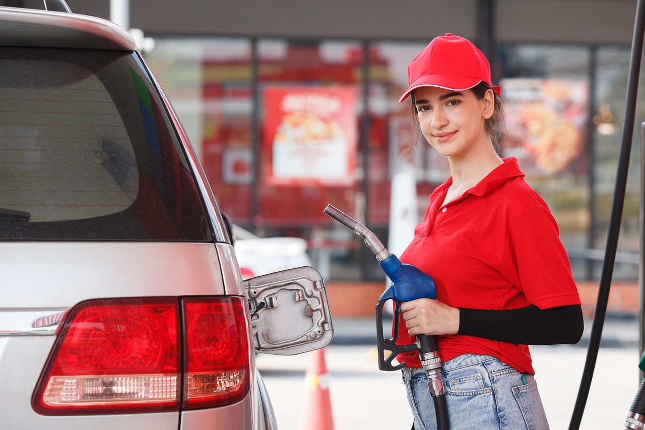 young caucasian woman red uniform holding fuel pump nozzle service refuel gas station. oil power energy automobile transport.
