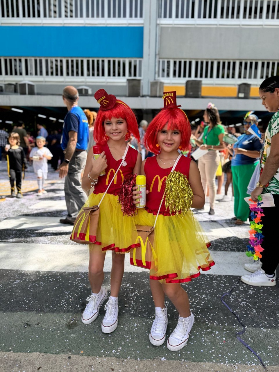 As garotas  saíram para a folia vestidas com uma camiseta vermelha, estampando o M da marca, saia amarela e peruca vermelha