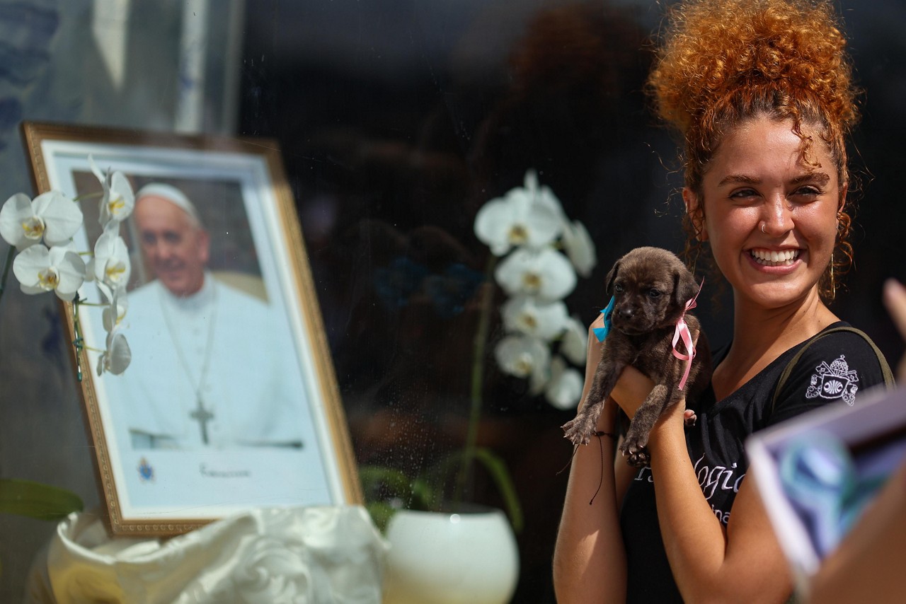 Gabriela Pedras, 22, segurando Carmela, sua nova companheira em frete a imagem do Papa Franciscona porta da Igreja da Pampulha