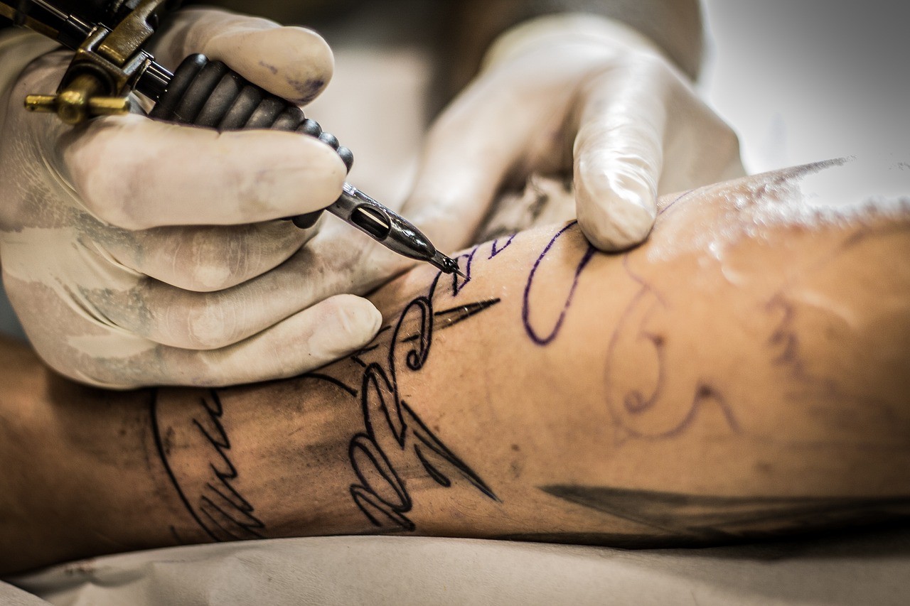 Imagem ilustrativa mostra tatuador fazendo um desenho na pele de uma pessoa