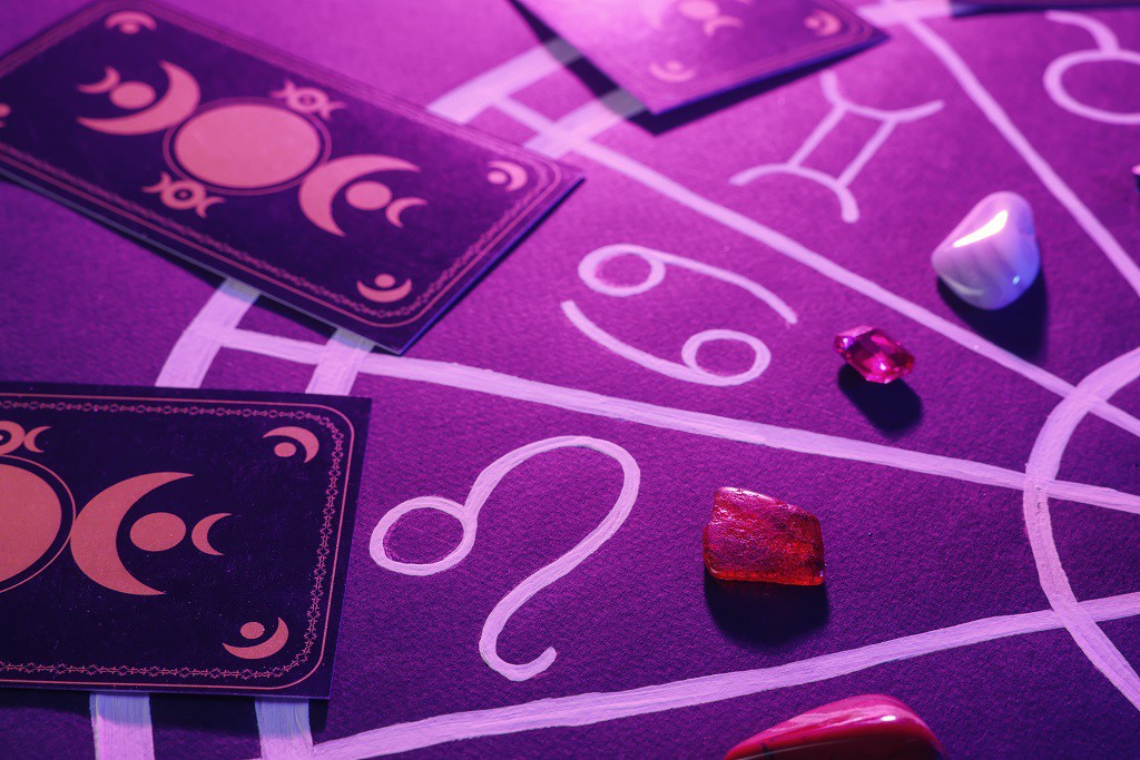 Natural stones for zodiac signs, tarot cards and drawn astrology chart on purple background, closeup. Color tone effect