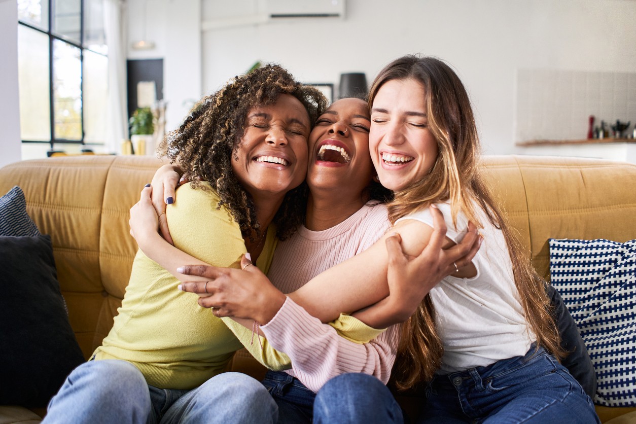 Three happy friends hugging smiling.Funny women together celebrating sitting on the living room sofa. High quality photo