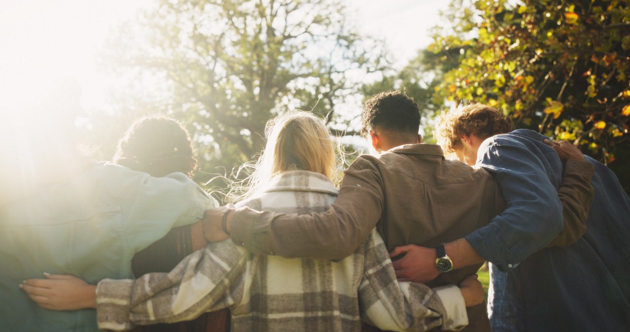 Group, back and friends to relax outdoor on school break, discussion and hug for bonding in summer. People, students and embrace with , care and trust together for social reunion at park