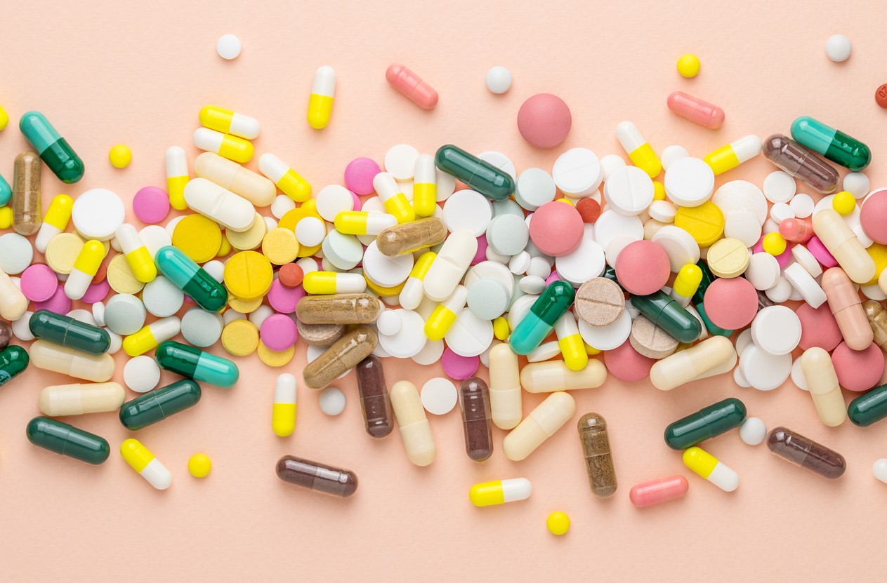Many different pills on pink background. Prescription pills and vitamins. Flat lay and space for text