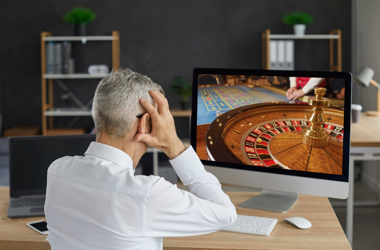 Unlucky old gambler places bet in online casino gambling game and loses all his money. Back view of senior man looking at desktop computer PC screen feeling desperate and holding his head in his hands