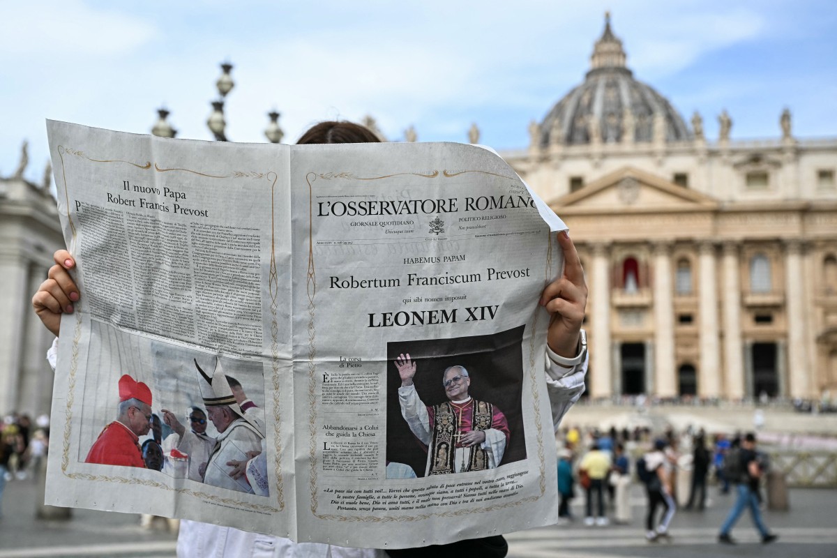 A woman reads L'Osservatore Romano newspaper with the front page picture of newly elected pope Leo XIV, on St Peter's Square with the St Peter's Basilica in the background in The Vatican on May 9, 2025. (Photo by Gabriel BOUYS / AFP)