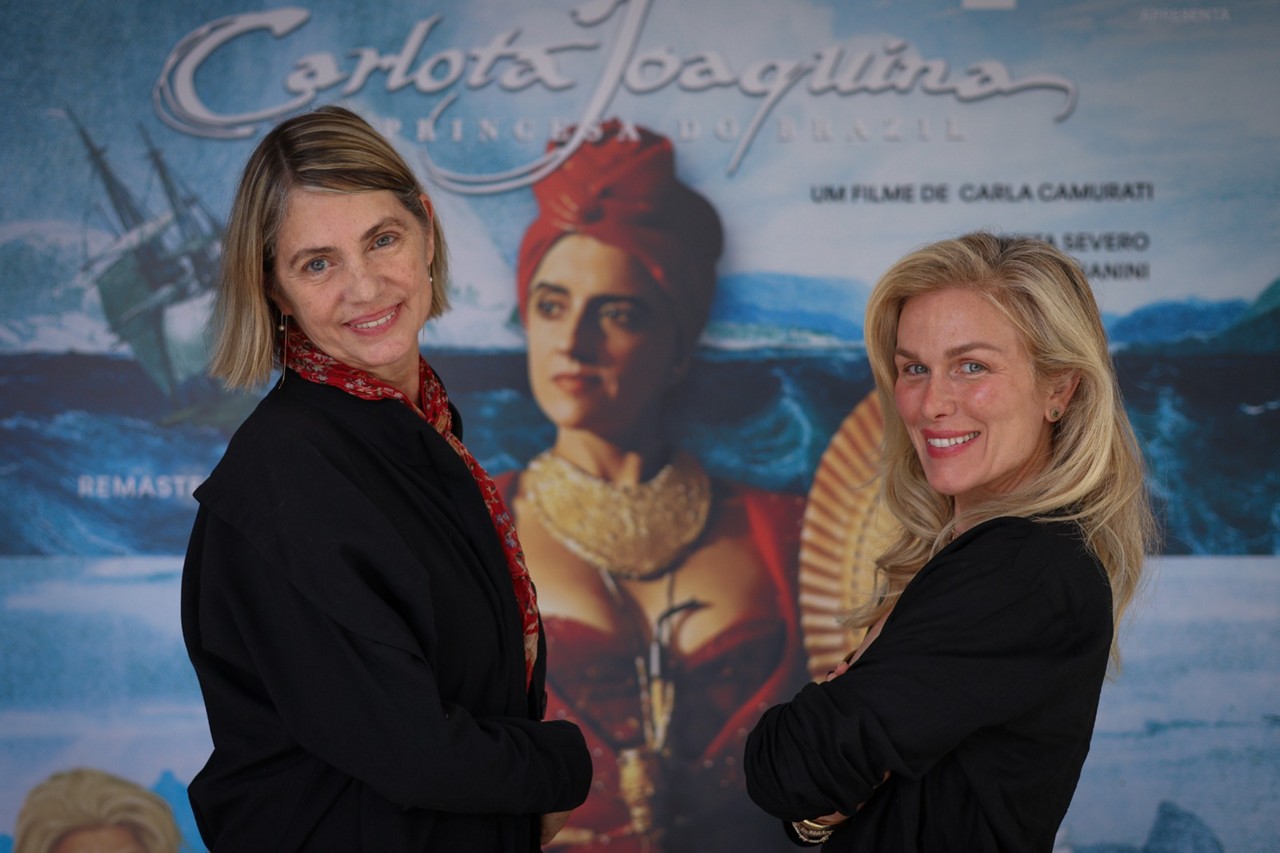 Carla Camurati e Ludmila Dayer à frente do cartaz do filme protagonizado por Marieta Severo