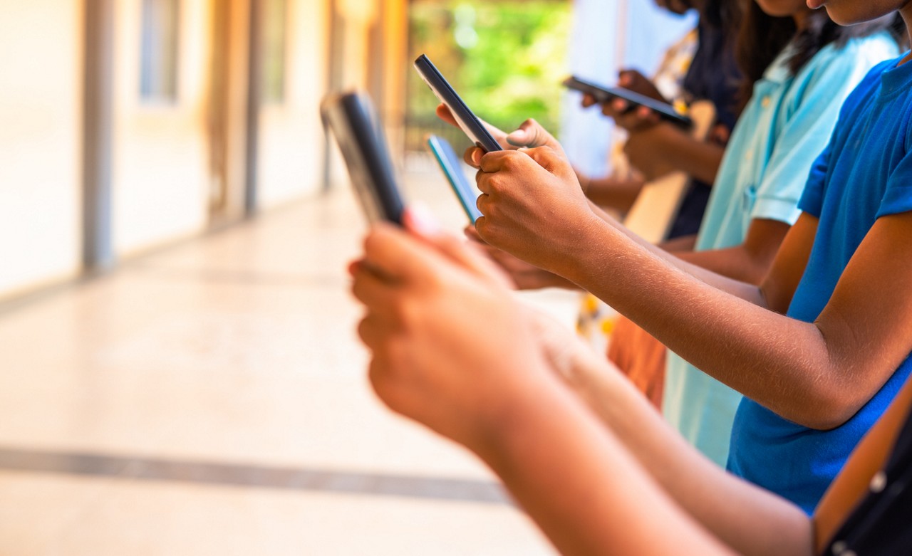 Close up shot, group of children hands busy using smartphone at school corridor - concept of social media, playing games, technology and education.