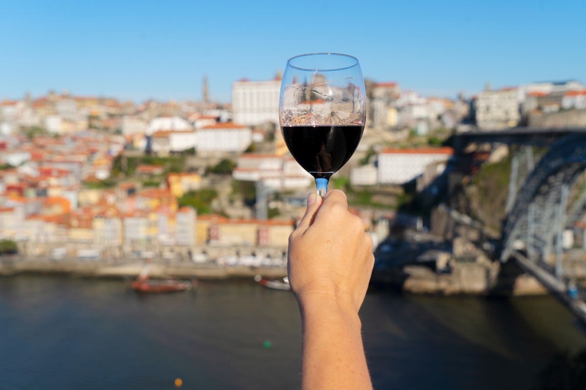 hand of woman with glass of ruby port wine on historic town of Porto, background Portugal