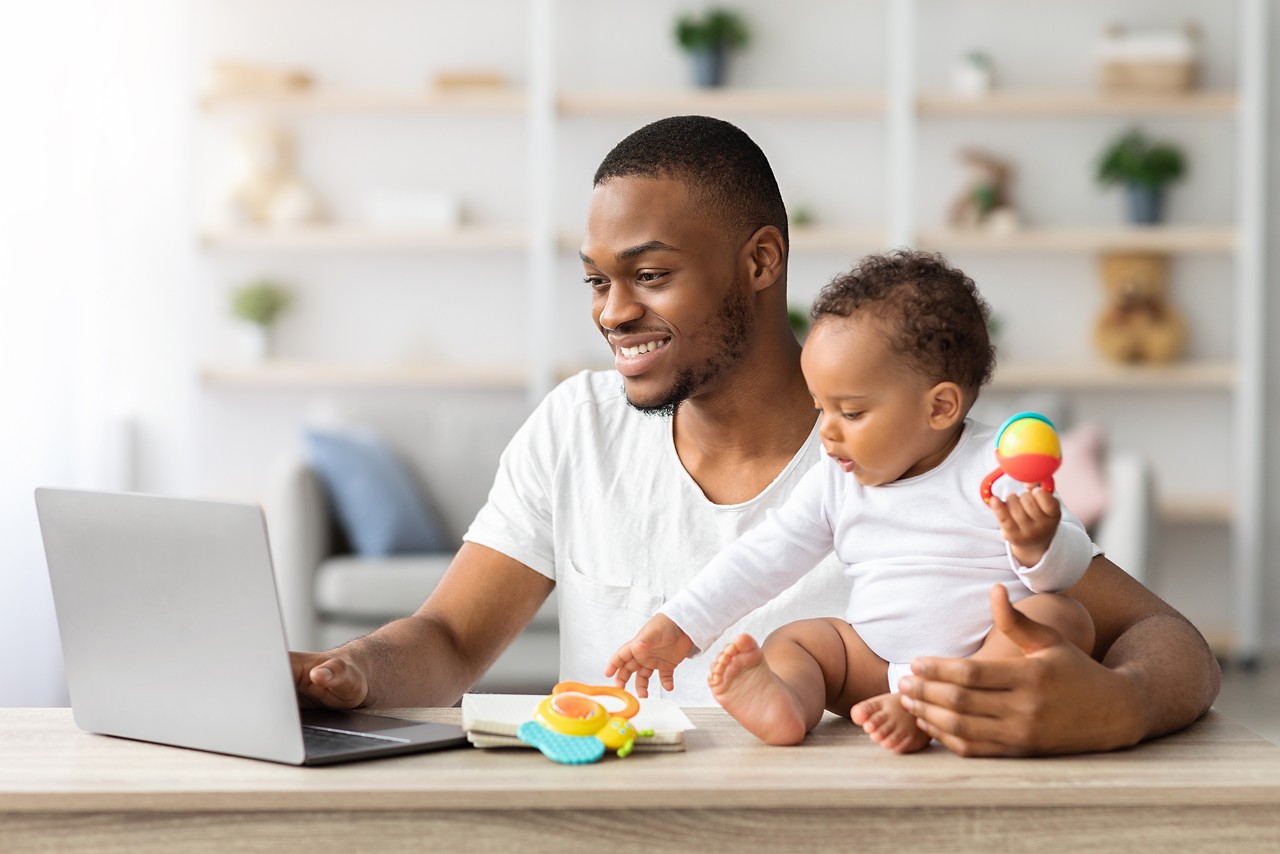 Paternity Leave. Black Man Using Laptop At Home And Babysitting Infant Child