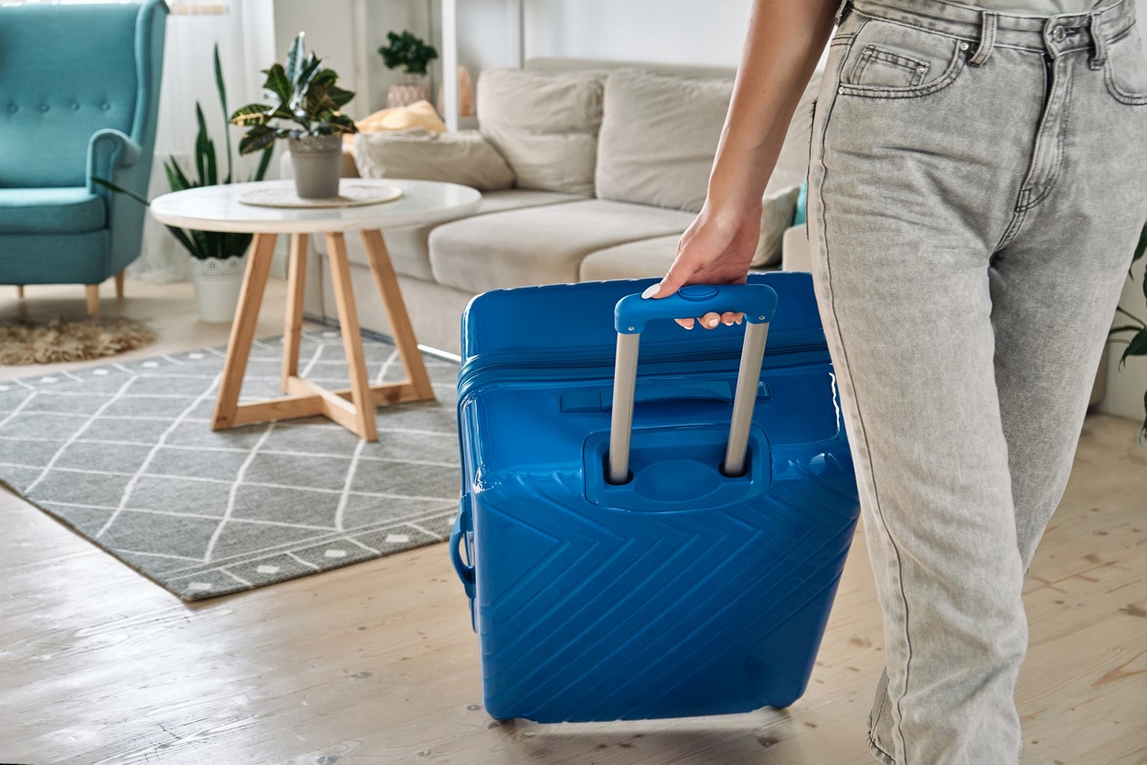 Unrecognizable woman leaving home with a suitcase going on a trip or vacation.