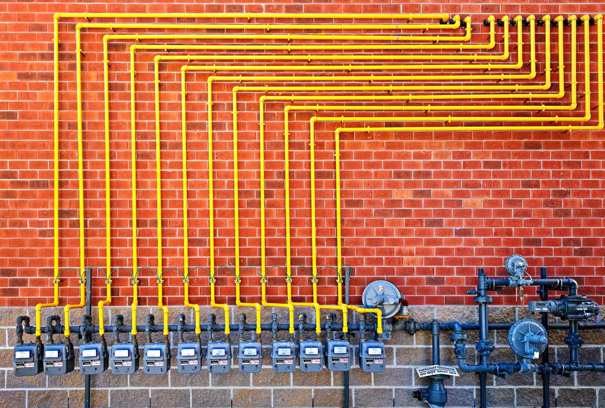 Row of natural gas meters with yellow pipes on building brick wall