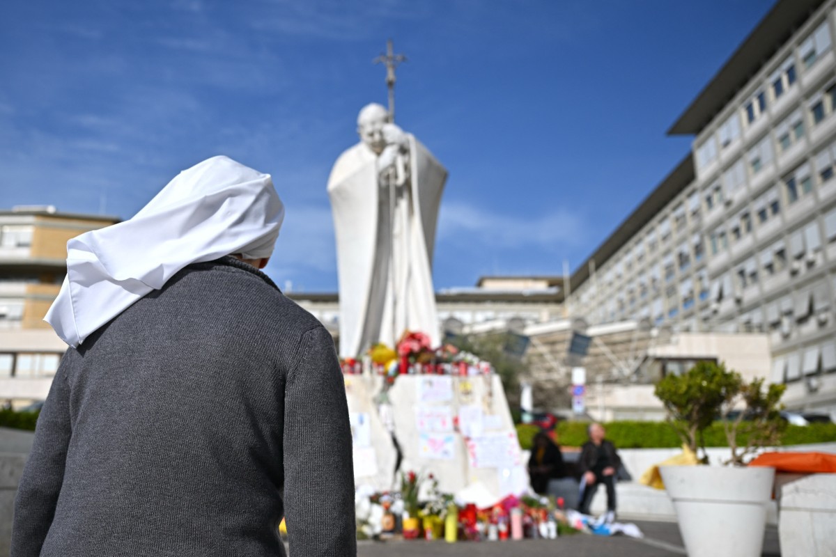 Uma freira reza na estátua do Papa João Paulo II do lado de fora do hospital Gemelli, onde o Papa Francisco está hospitalizado com pneumonia, em Roma, em 21 de março de 2025