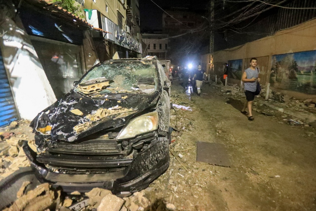 Homens passam por destroços e um carro destruído após os andares superiores de um prédio de oito andares terem sido destruídos por ataque israelense em Beirute