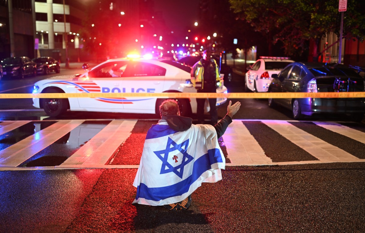 Homem com uma bandeira israelense gesticula enquanto policiais protegem a área em frente ao Museu Judaico da Capital após o ataque 