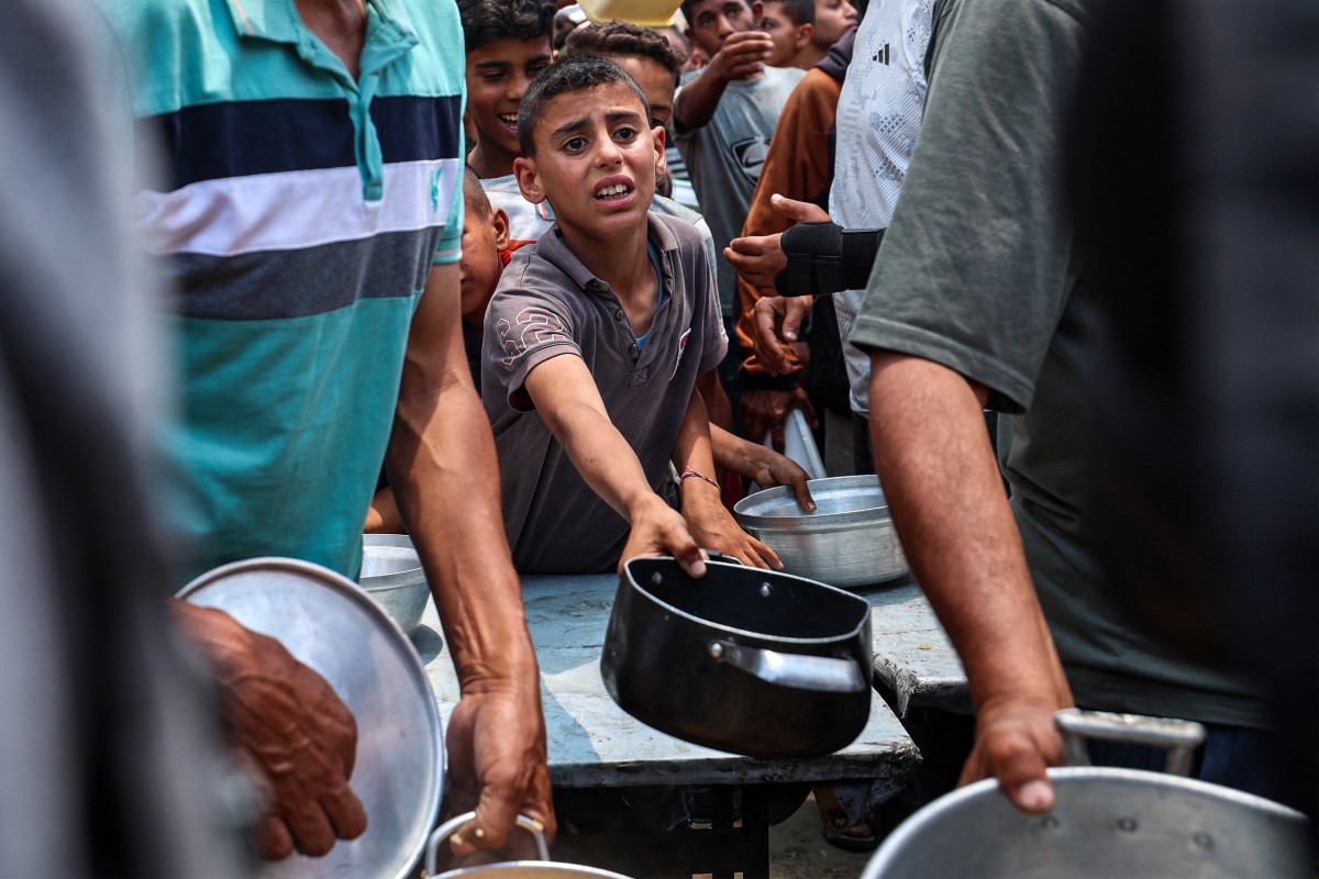 Palestinos se reúnem para receber uma refeição quente em um ponto de distribuição de alimentos no campo de refugiados