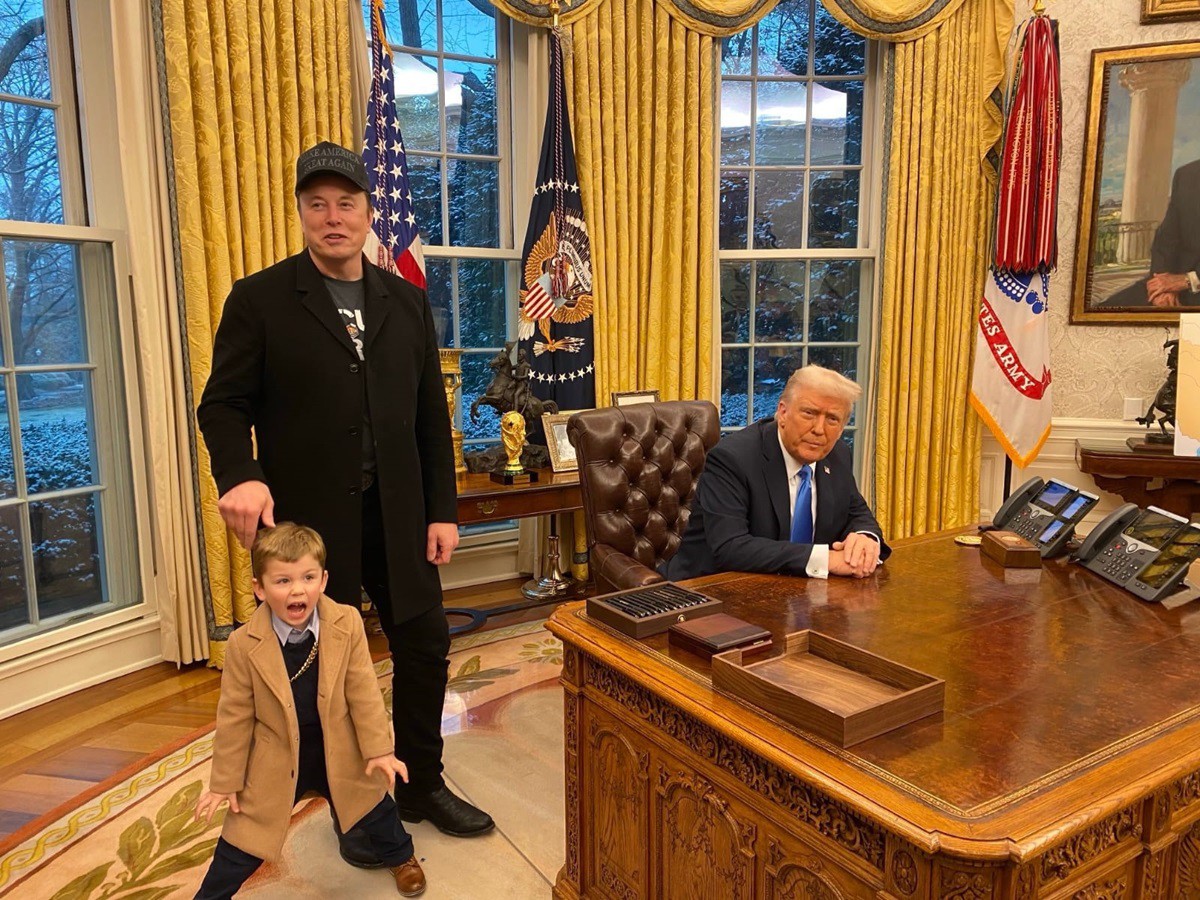 Elon Musk (de preto, em pé), que é secretário no governo de Donald Trump (sentado), questionou em post no X se o ministro do STF Alexandre de Moraes tem bens nos Estados Unidos