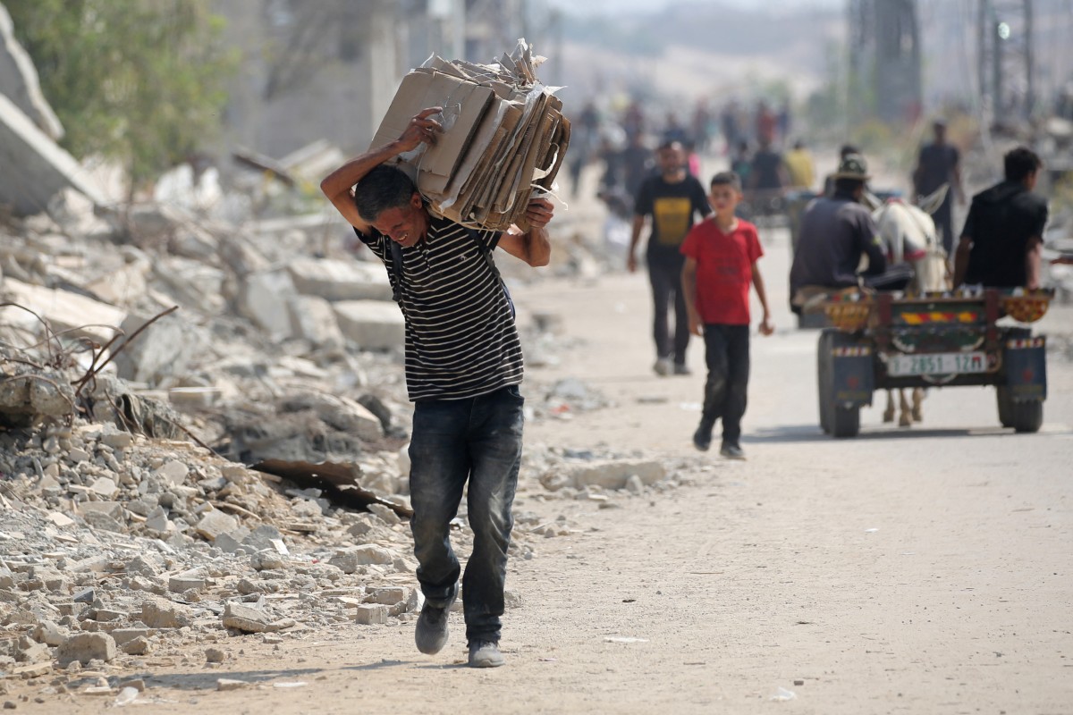 Palestinos deslocados no campo de refugiados de Nuseirat carregam pacotes de alimentos e outros itens que conseguiram obter em um ponto de distribuição de ajuda da GHF no chamado “corredor de Netzarim”, na região central da Faixa de Gaza