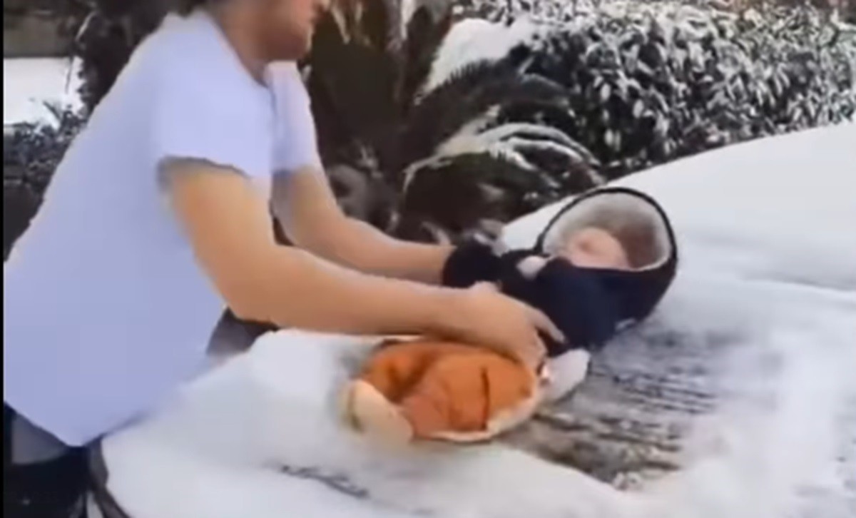 Vídeo mostra bebê arrastado por homem para limpar neve de carro