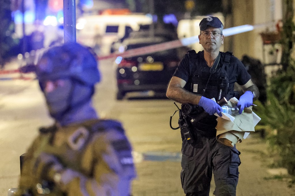 A member of the Israeli police's forensics department walks past a special forces member at the scene of a shooting attack in Jaffa south of Tel Aviv on October 1, 2024. At least four people were shot dead on October 1 in a suspected attack in Israel's central city of Tel Aviv, police said, adding that the two assailants had been "neutralised". (Photo by Jack GUEZ / AFP)