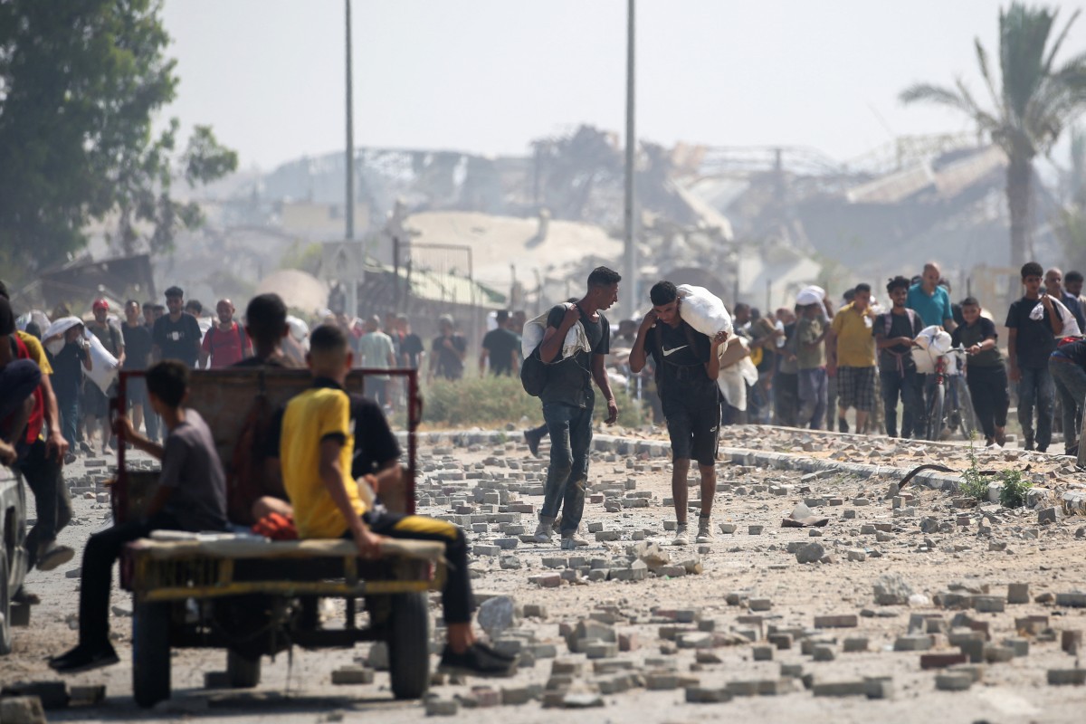 Palestinos deslocados no campo de refugiados de Nuseirat carregam pacotes de alimentos e outros itens que conseguiram obter em um ponto de distribuição de ajuda da GHF no chamado "corredor de Netzarim", na região central da Faixa de Gaza
