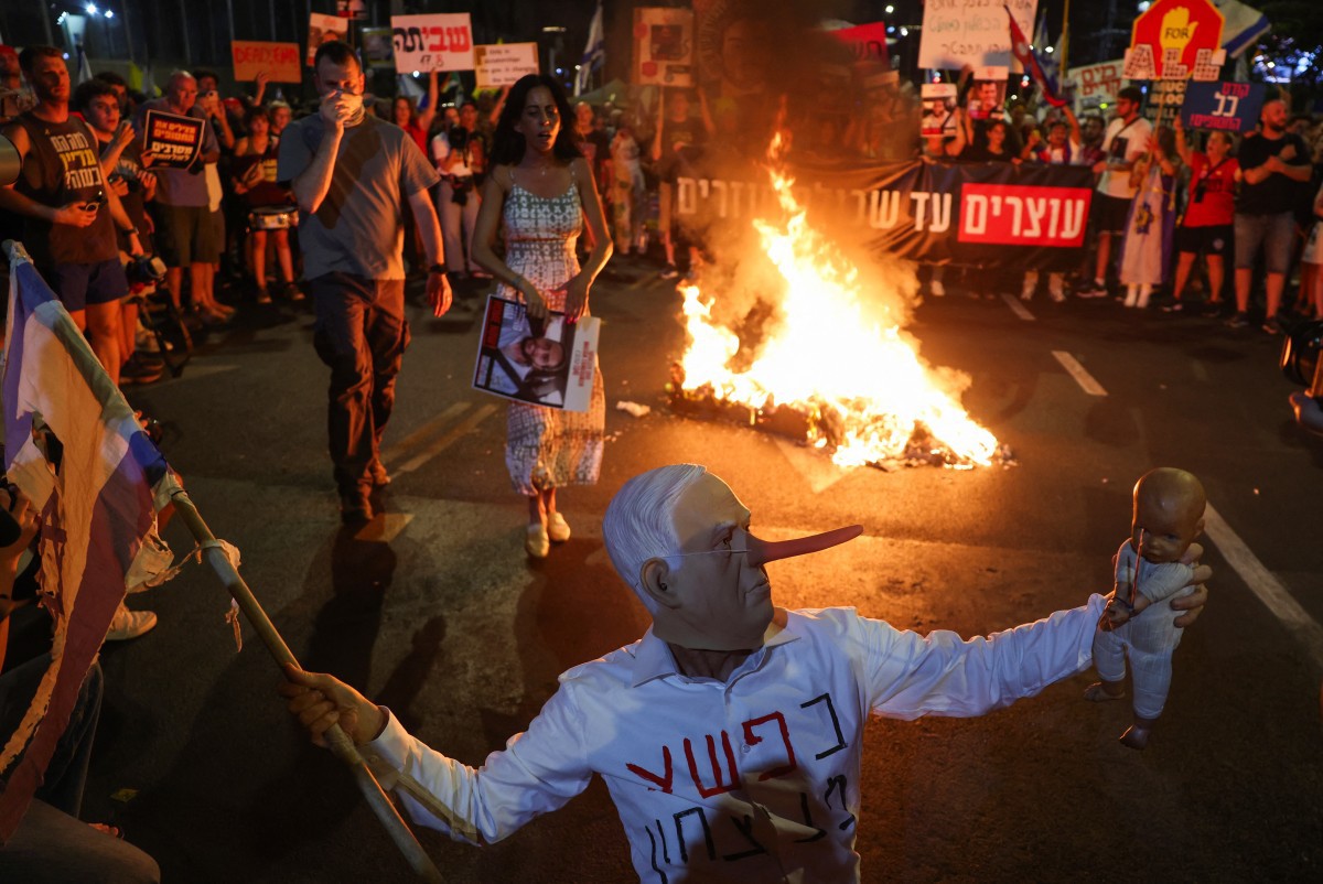 Um manifestante usando uma máscara representando o primeiro-ministro israelense Benjamin Netanyahu faz um gesto durante um ato em uma manifestação organizada pelas famílias dos reféns mantidos por militantes palestinos em Gaza desde 2023