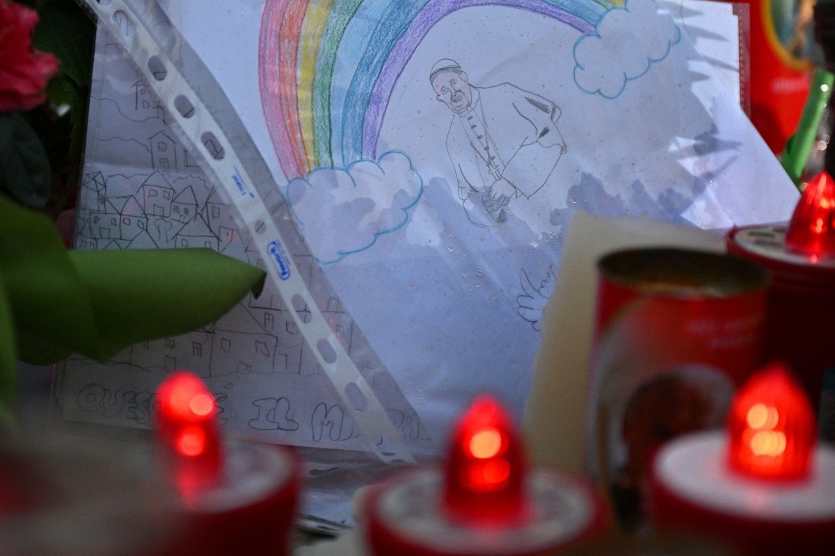 A drawing depicting Pope Francis under a rainbow is laid at the statue of John Paul II outside the Gemelli hospital where Pope Francis is hospitalized with pneumonia, in Rome on March 14, 2025.  (Photo by Alberto PIZZOLI / AFP)