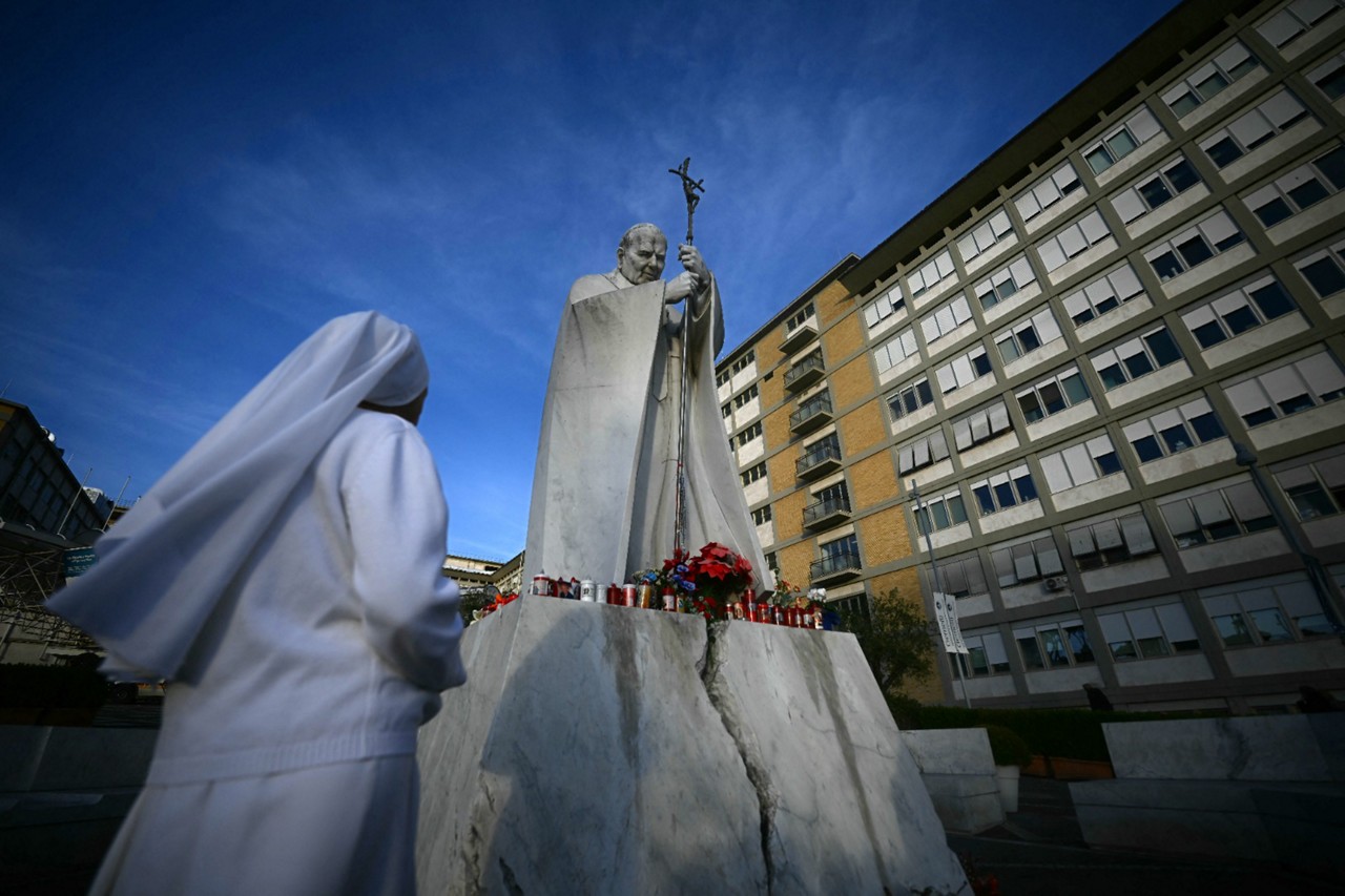 Pessoas diante de uma estátua do Papa João Paulo II em frente ao hospital Gemelli