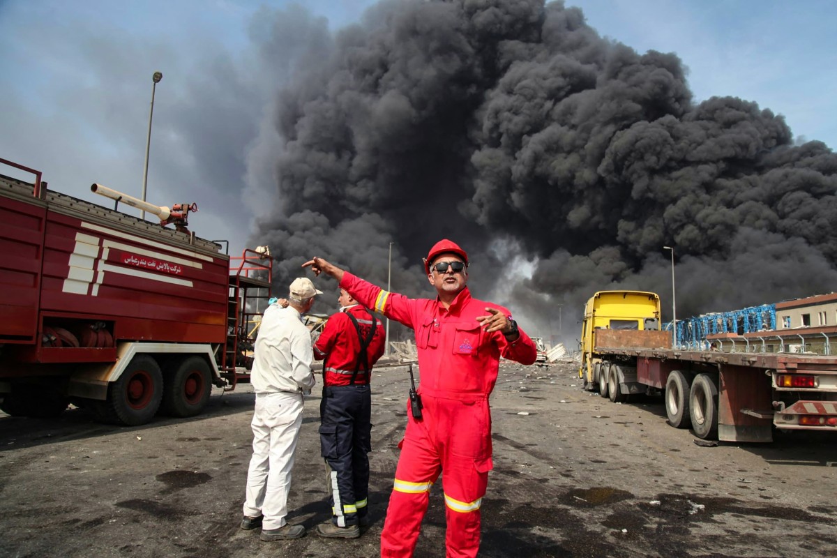 Funcionário do porto Shahid Rajaee, no Irã, tenta afastar pessoas do local da explosão (Photo by MOHAMMAD RASOLE MORADI  IRNA  AFP)