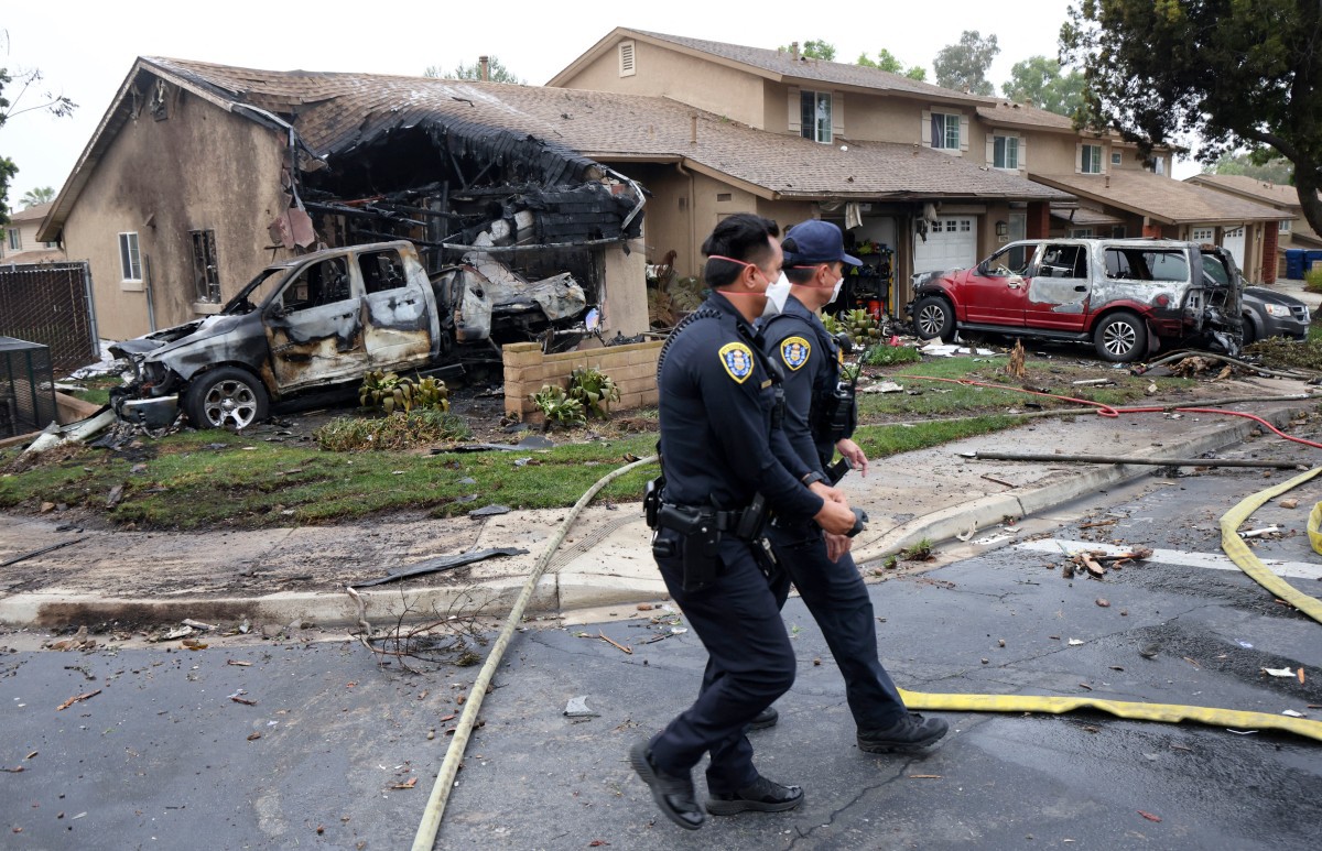 Policiais caminham diante de casa atingida pela queda de avião em bairro de San Diego, na Califórnia