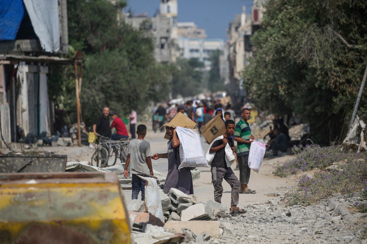Palestinos deslocados no campo de refugiados de Nuseirat transportam pacotes de alimentos e outros itens que conseguiram obter de um ponto de distribuição de ajuda