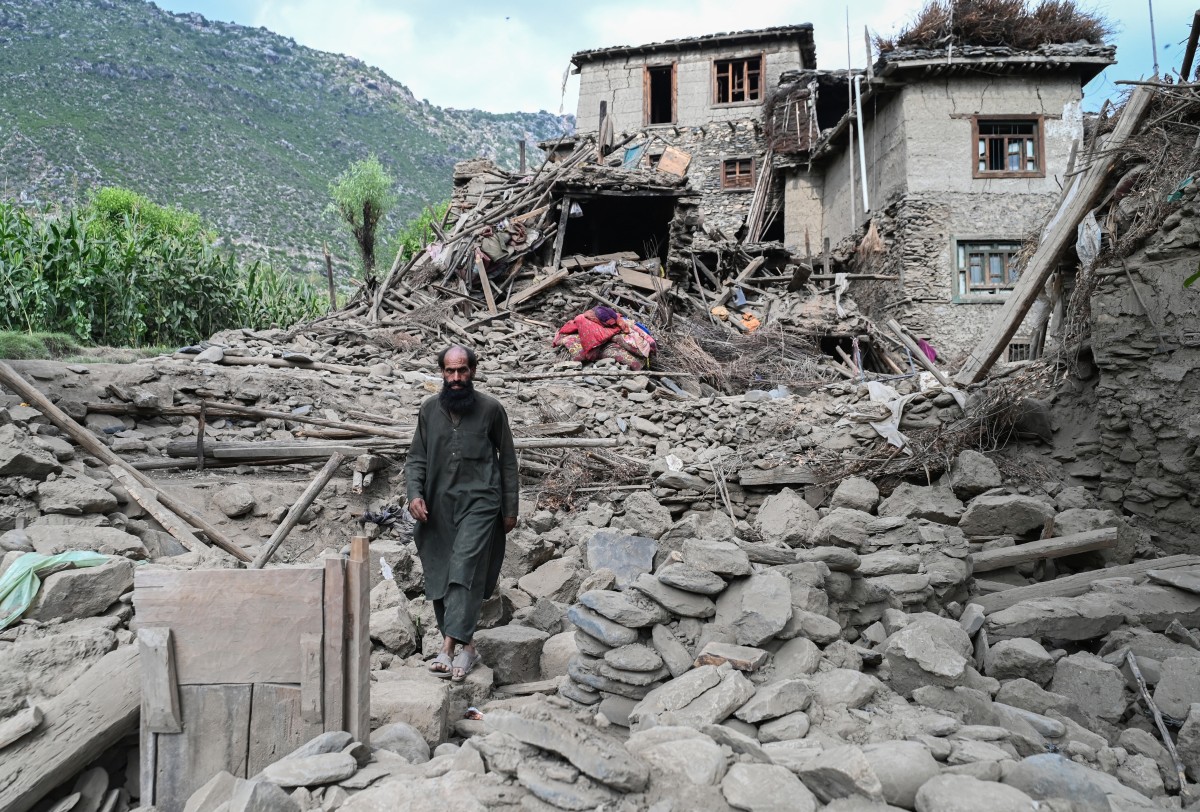 Um afegão caminha em frente a uma casa destruída após terremotos na vila de Mazar Dara, em Nurgal, ao leste do Afeganistão