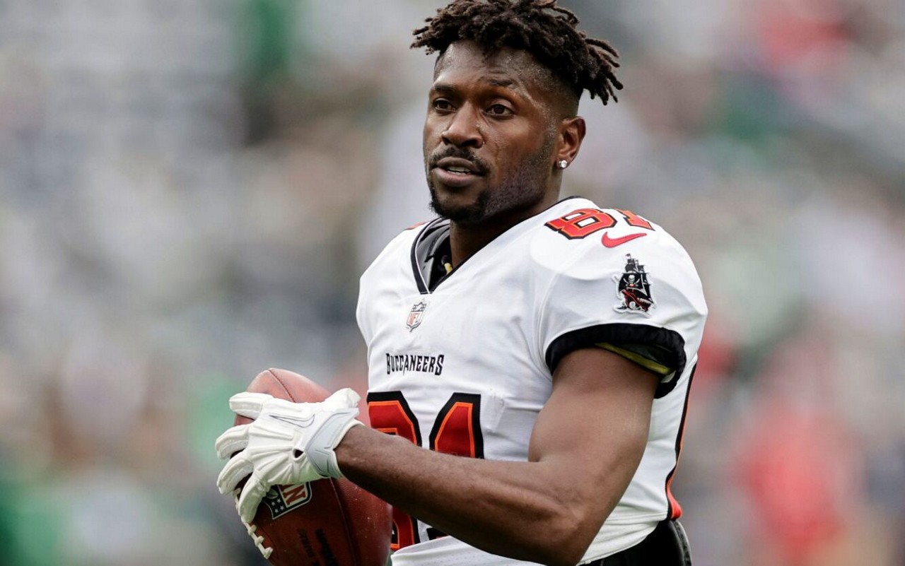 Antonio Brown, ex-NFL, preocupado, usando o uniforme dos Buccaneers e segurando uma bola de futebol americano