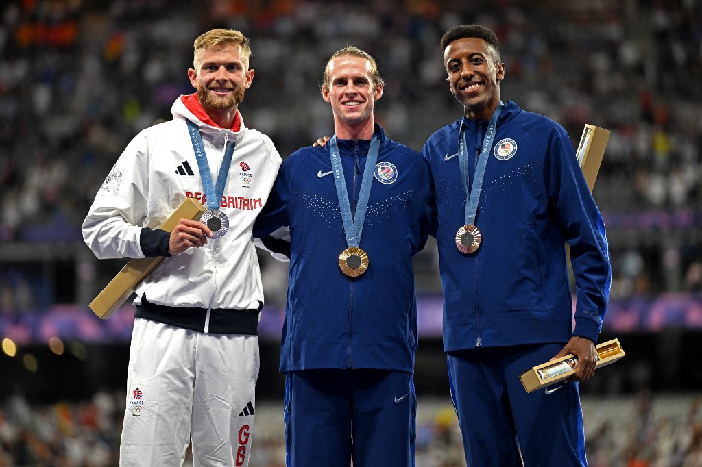 Silver medallist Britain's Josh Kerr (L), gold medallist US' Cole Hocker (C) and bronze medallist US' Yared Nuguse celebrate on the podium during the victory ceremony for the men's 1500m athletics event during the Paris 2024 Olympic Games at Stade de France in Saint-Denis, north of Paris, on August 6, 2024. (Photo by MARTIN BERNETTI / AFP)