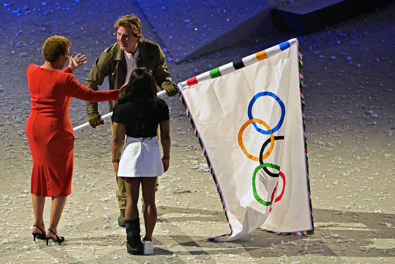 O ator norte-americano Tom Cruise recebe a bandeira olímpica das mãos da prefeita de Los Angeles, Karen Bass, e da ginasta norte-americana Simone Biles, durante a cerimônia de encerramento dos Jogos Olímpicos Paris 2024