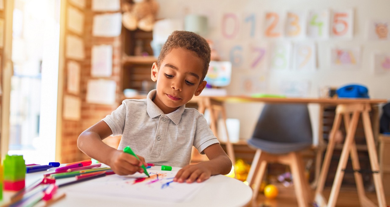 Beautiful african american toddler drawing using paper and marker pen at kindergarten