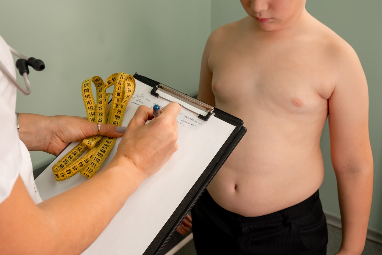 Friendly nutritionist measures waist. Childhood obesity and weight loss. Overweight boy consulting with doctor in office. Doctor examining fat boy in clinic. Doctor measuring overweight boy.