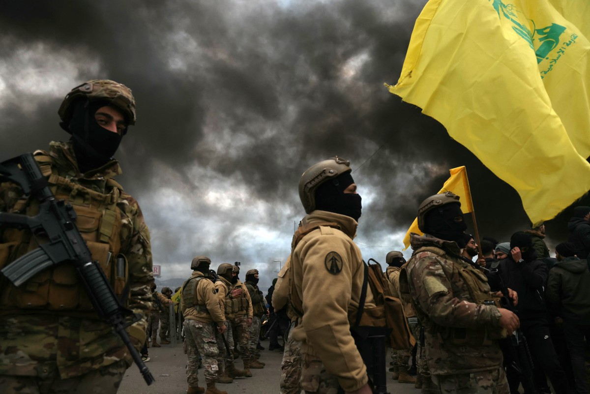Apoiadores do Hezbollah agitam a bandeira do grupo em frente a tropas do exército libanês, enquanto manifestantes queimam pneus para bloquear a estrada que leva ao aeroporto internacional de Beirute, após a visita da enviada especial adjunta dos EUA para o Oriente Médio, Morgan Ortagus, durante a qual ela se reuniu com o presidente do país, em fevereiro de 2025