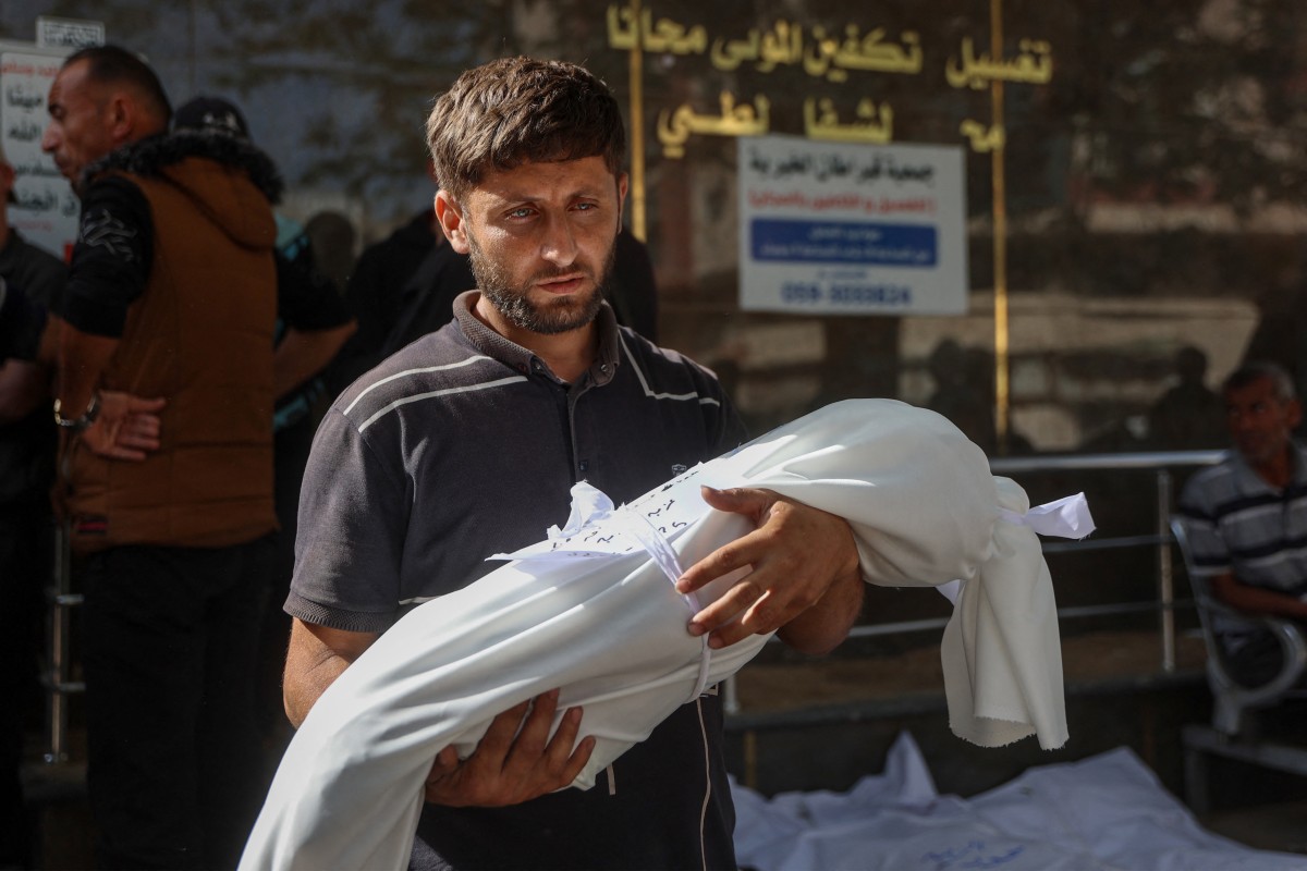 Homem carrega corpo de criança morta durante ataque de Israel a um hospital da Faixa de Gaza, em 26 de maio de 2025
