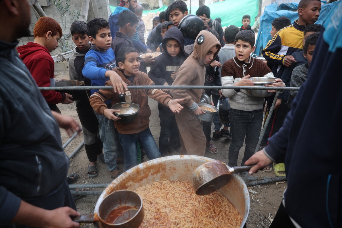 Crianças palestinas esperam por uma refeição durante a distribuição de alimentos no campo de refugiados de Nuseirat, no centro da Faixa de Gaza, em 3 de março de 2025, durante o mês sagrado de jejum muçulmano do Ramadã