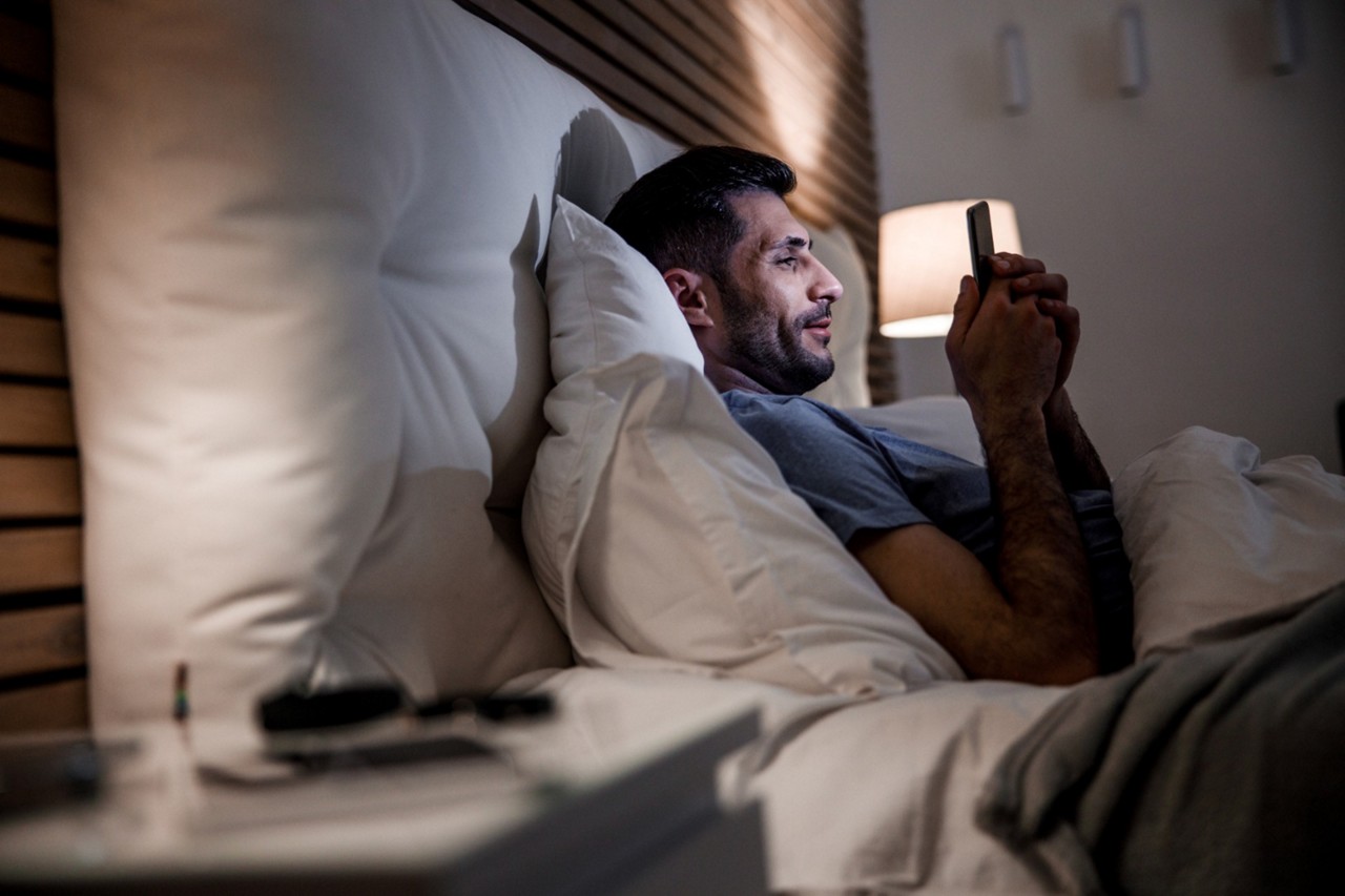 Homem preparado para dormir, já na cama, mexe em celular