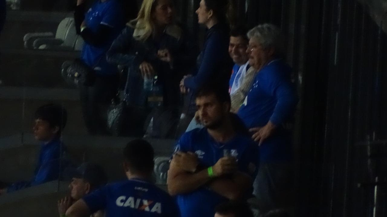Itair Machado, de branco, está em um camarote do Mineirão, onde acompanha o duelo entre Cruzeiro e River Plate
