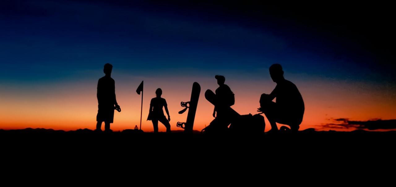 Praticantes de sandboard contemplam o pôr so sol na Duna Mãe