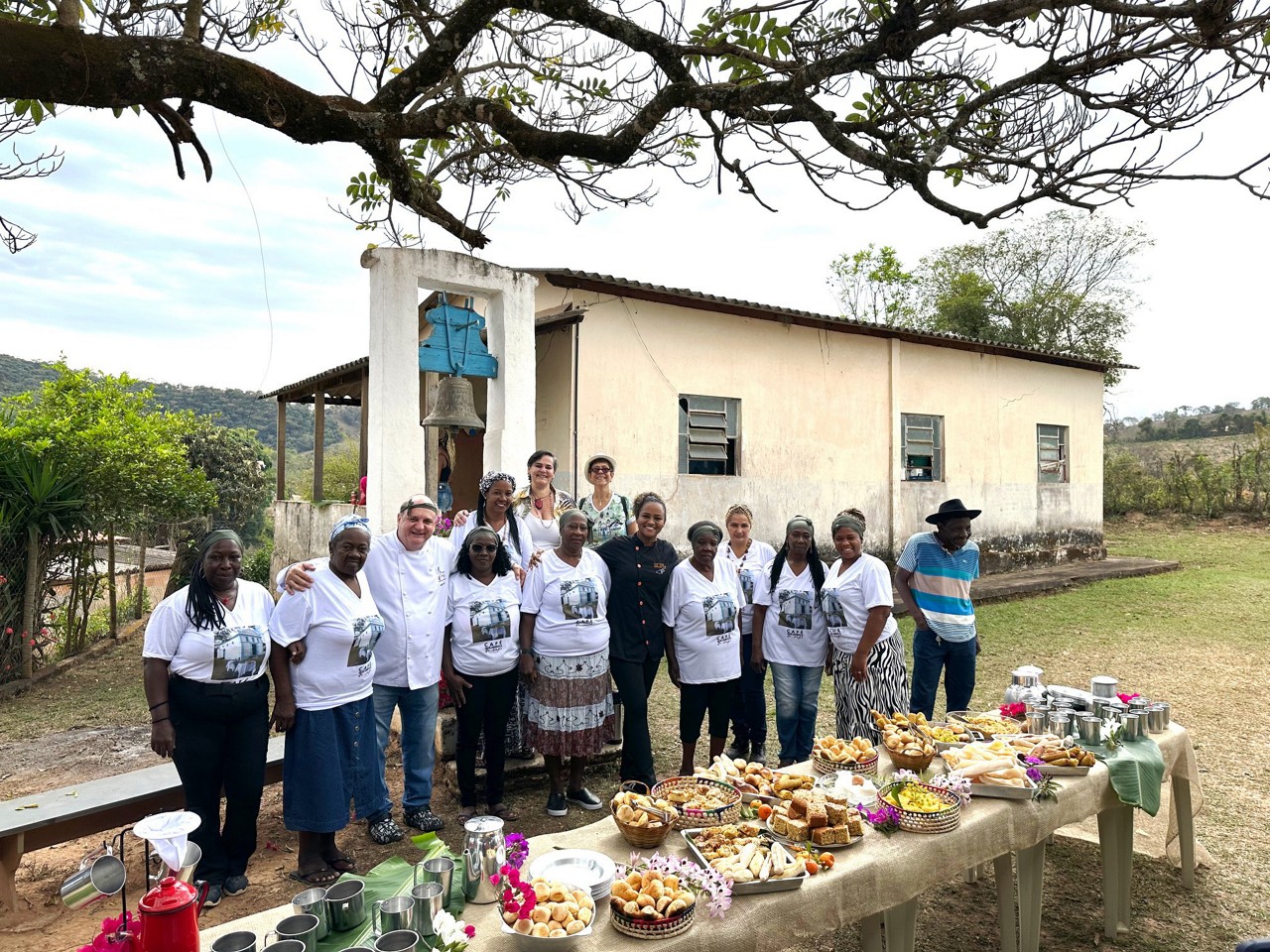 O chef Edson  Puiati e os  membros da comunidade quilombola de Sapé reunidos em torno de uma mesa de café da manhã com quitandas para receber os visitantes