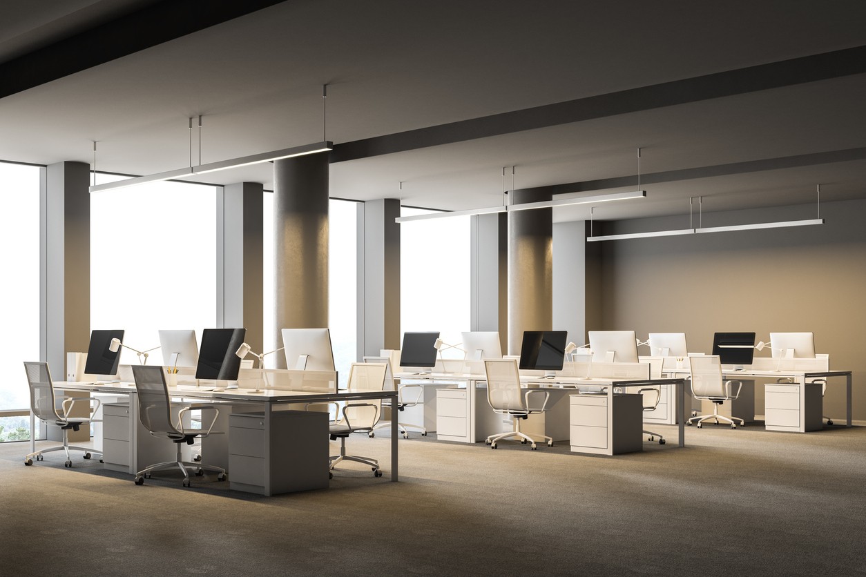 Side view of a spacious gray wall office interior with a concrete floor, columns and rows of computer tables. 3d rendering mock up